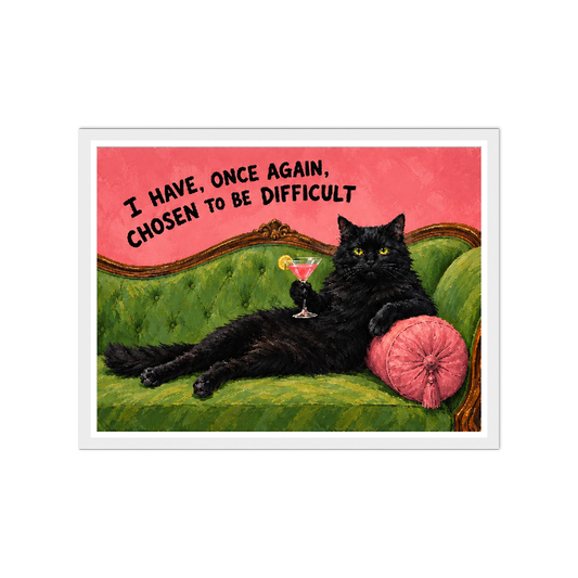 Black cat with a cocktail on a green sofa beneath a chosen to be difficult quote in a white frame.