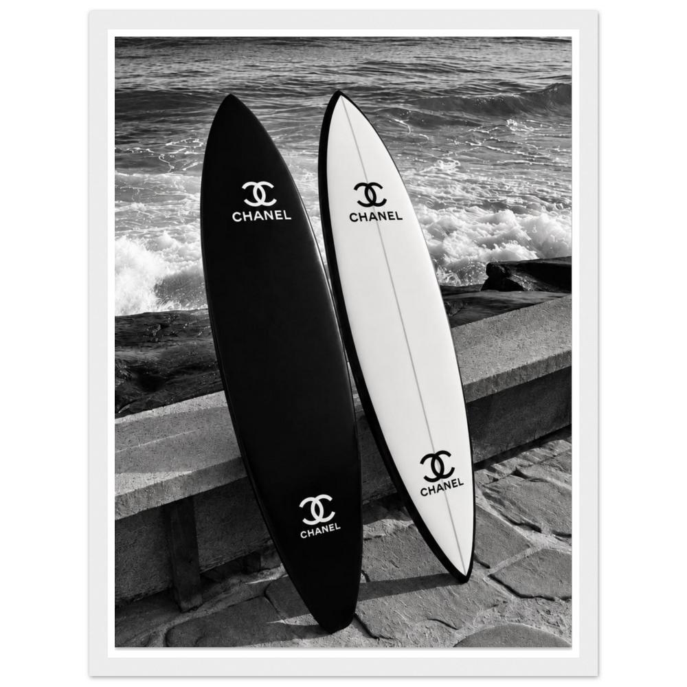 Black and white surfboards leaning against a sea wall beside the waves in a white frame.