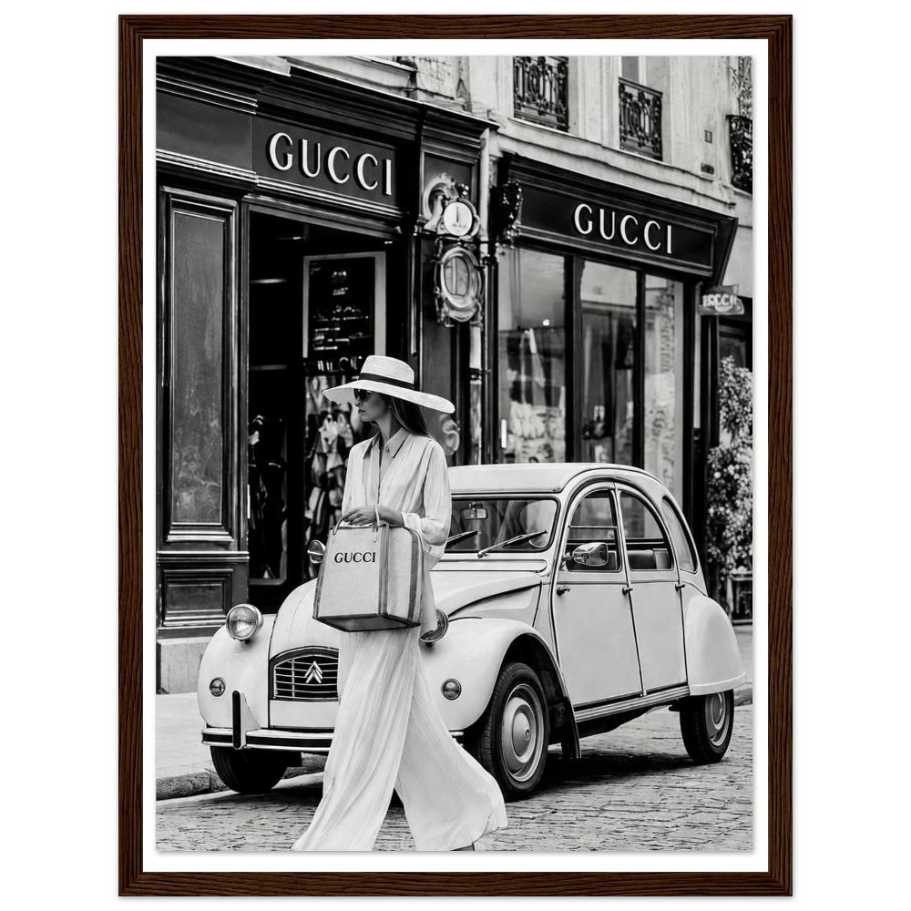 Woman in a sunhat walking past a vintage car outside a boutique in black and white in a dark wood frame.