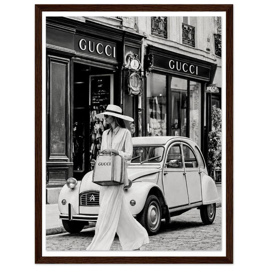 Woman in a sunhat walking past a vintage car outside a boutique in black and white in a dark wood frame.
