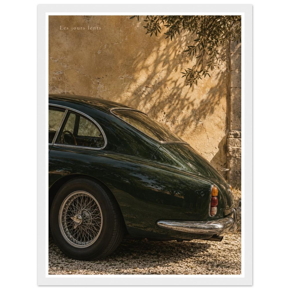 Deep green classic car beside a sunlit ochre wall with leafy shadows in a white frame.