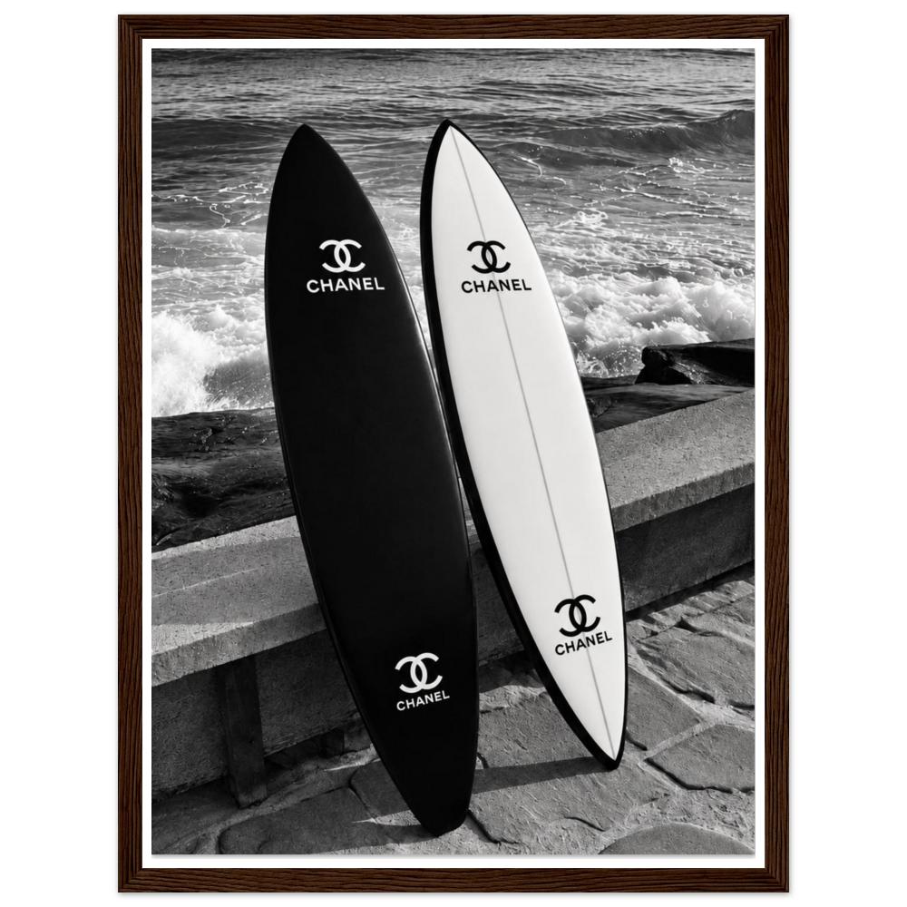 Black and white surfboards leaning against a sea wall beside the waves in a dark wood frame.