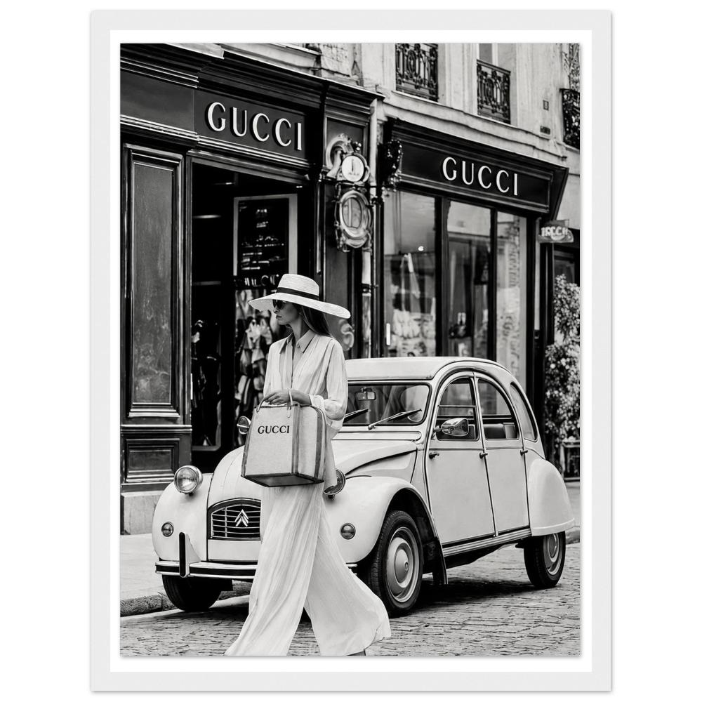 Woman in a sunhat walking past a vintage car outside a boutique in black and white in a white frame.
