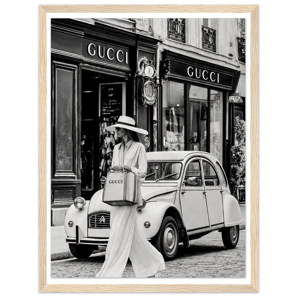 Woman in a sunhat walking past a vintage car outside a boutique in black and white in a natural wood frame.
