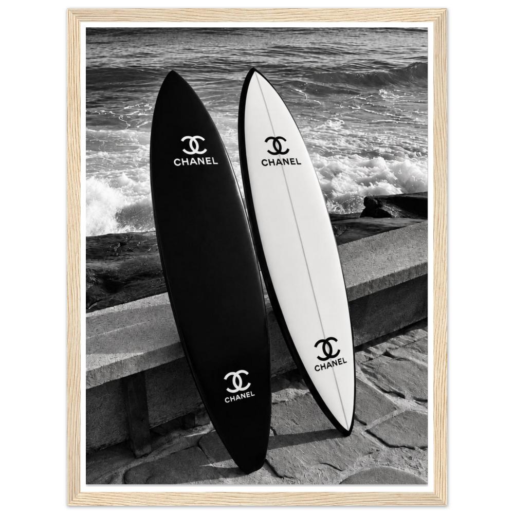 Black and white surfboards leaning against a sea wall beside the waves in a natural wood frame.