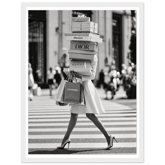 Woman crossing a street in heels carrying a tall stack of shopping boxes in a white frame.
