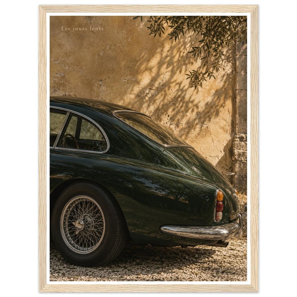 Deep green classic car beside a sunlit ochre wall with leafy shadows in a natural wood frame.