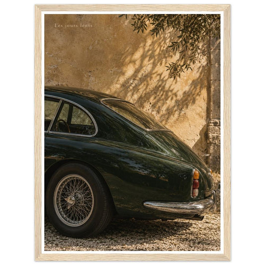 Deep green classic car beside a sunlit ochre wall with leafy shadows in a natural wood frame.