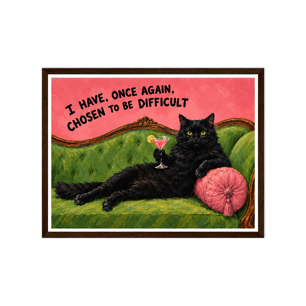Black cat with a cocktail on a green sofa beneath a chosen to be difficult quote in a dark wood frame.