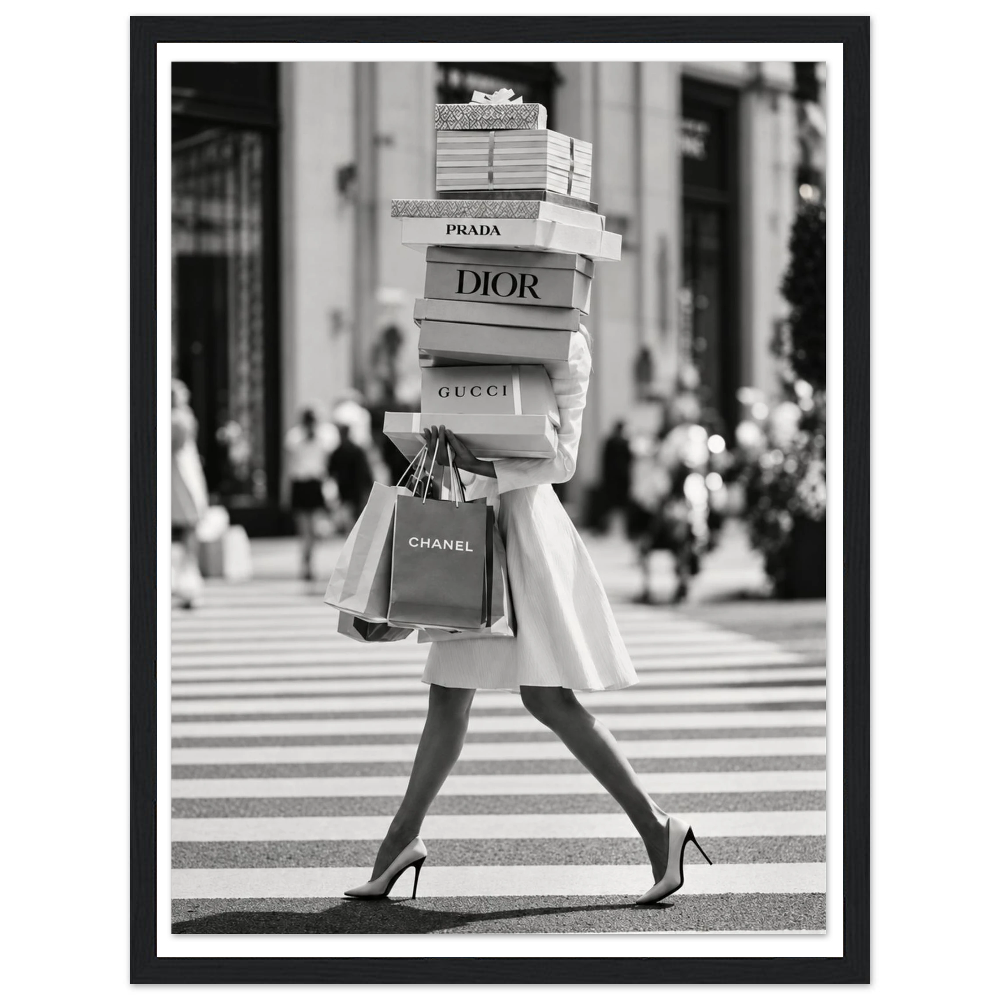 Woman crossing a street in heels carrying a tall stack of shopping boxes in a black frame.