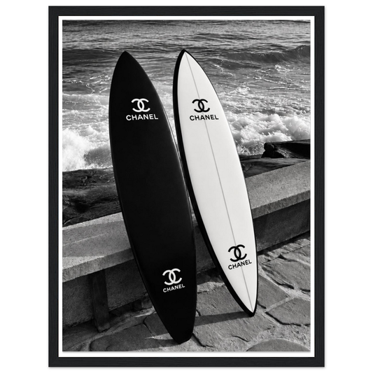 Black and white surfboards leaning against a sea wall beside the waves in a black frame.