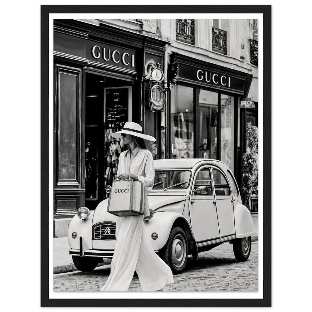 Woman in a sunhat walking past a vintage car outside a boutique in black and white in a black frame.