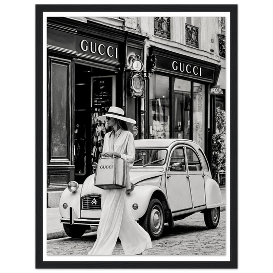 Woman in a sunhat walking past a vintage car outside a boutique in black and white in a black frame.